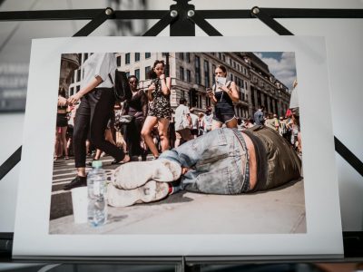 Print van voorbijgangers die kijken naar een dakloze man die kennelijk onverstoorbaar op de stoep ligt te slapen in Regent Street in Londen.