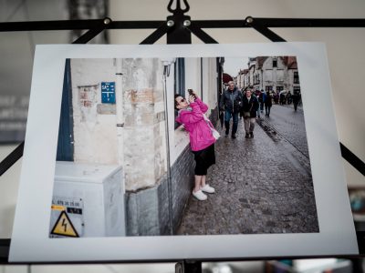 Print van een foto waarop een Aziatische toeriste met haar mobiele telefoon een foto maakt van het Sint-Janshospitaal in Brugge.