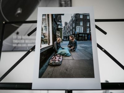 Print of a photo in which a young woman is talking with compassion to another rough sleeping woman of equal age in the centre of the English city of York.